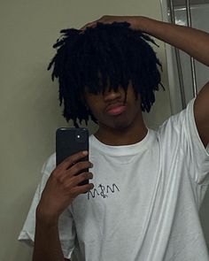 a young man with dreadlocks is looking at his cell phone in the mirror