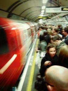 a crowd of people standing next to a red train at a subway station in the city