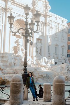 a woman standing next to a lamp post in front of a building with statues on it