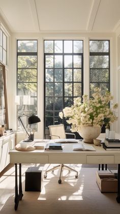 a white desk in front of two large windows and a vase with flowers on it