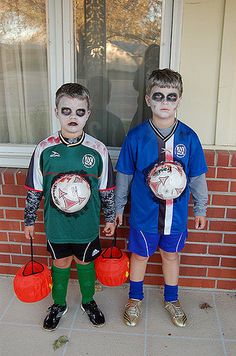 two young boys dressed up as soccer players with their faces painted like they are holding orange buckets