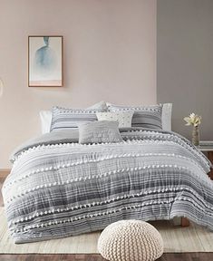 a bed with grey and white comforter in a room next to a painting on the wall