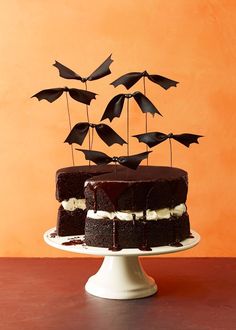 a chocolate cake topped with black bats on top of a wooden table next to an orange wall