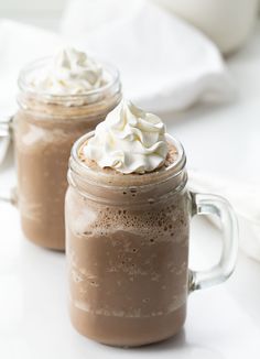 two mugs filled with hot chocolate and whipped cream sitting on a white counter top