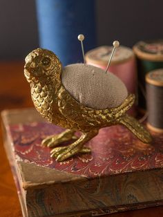 a golden owl figurine sitting on top of a book with thread spools