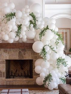 a living room filled with white balloons and greenery hanging from the ceiling next to a fire place