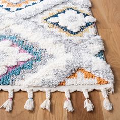 a multicolored rug with tassels and fringe on the floor next to a wooden floor