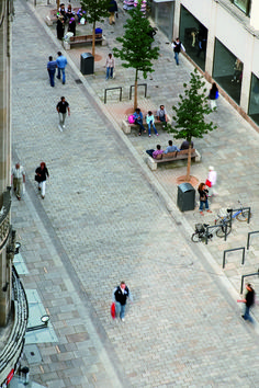 many people are walking around on the sidewalk in an open area with stone pavers