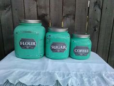 three green mason jars sitting on top of a white table cloth next to a wooden fence