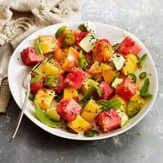 a white bowl filled with fruit salad next to a fork and napkin on top of a table