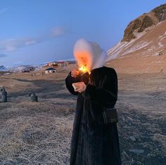 a woman in a long black dress and white hat is holding a lit up candle