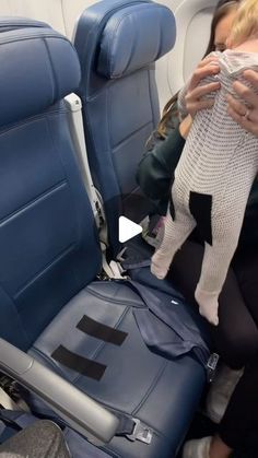 a woman holding a baby in her arms while sitting on an airplane with the seat back down