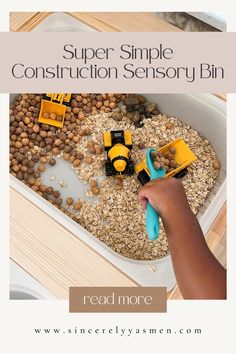 a child's hand is playing with construction toys in a play tray filled with oats