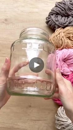 someone is holding a jar with yarn in it on the floor next to a wooden table