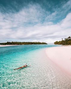 a person is floating in the clear blue water near an island with white sand and palm trees