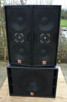 two speakers are stacked on top of each other in front of some trees and bushes