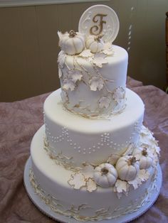 a three tiered cake with white frosting and flowers on the side, topped with a monogram