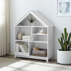 a house shaped shelf with books and plants on it next to a potted cactus