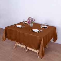 the table is set for two with plates and wine glasses on it in front of a white wall