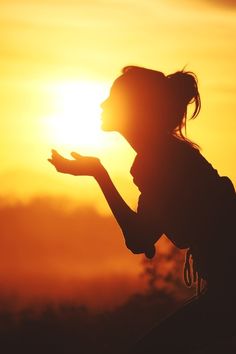 the silhouette of a woman holding her hand out in front of the sun on a foggy day