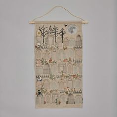 an embroidered wall hanging with birds, trees and buildings in the background on a gray wall