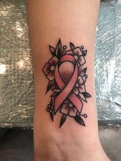 a pink ribbon tattoo on the foot of a woman's left leg with flowers around it