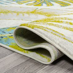 an area rug with yellow, blue and white designs on the carpet is laying on top of a wooden floor