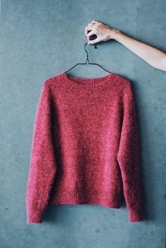 a red sweater hanging on a hanger next to a person's hand holding it