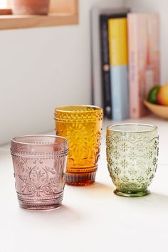 three different colored glass cups sitting on top of a white counter next to bookshelves