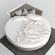 a round bed with white sheets and pillows on top of it, next to a gray rug