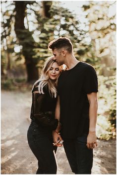 a man and woman standing next to each other in the woods with trees behind them