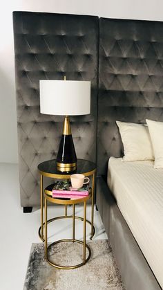 a black and gold table with a white lamp on it in front of a bed