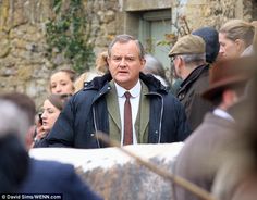 a man in a suit and tie standing next to a stone wall with people looking on