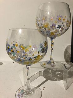 two wine glasses sitting on top of a table next to each other with flowers painted on them