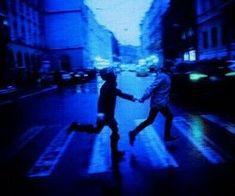 two people walking across a crosswalk in the dark with blue light shining on them