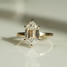 a close up view of a diamond ring on a white surface with the reflection of it's face