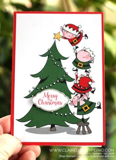 a hand holding up a christmas card with two pigs on top of a green tree