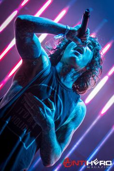 a man with long hair holding a microphone up to his head in front of neon lights