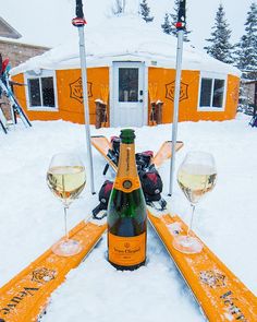 two glasses of wine sitting on top of snow covered ground with skis and poles