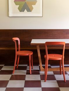 two orange chairs sitting next to each other in front of a painting on the wall