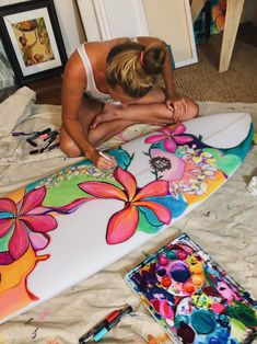 a woman is painting a surfboard with flowers on the bottom and sides in bright colors