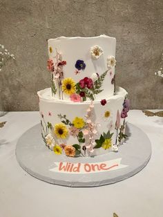 a three tiered cake decorated with flowers and wildflowers on a white table