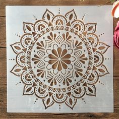 an intricately designed paper cutout on a wooden surface with purple flowers in the background