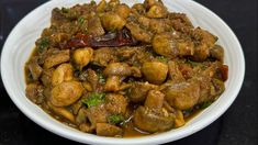 a white bowl filled with meat and vegetables on top of a black tablecloth covered table