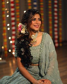 a woman sitting on the floor wearing a blue dress and flower in her hair, smiling at the camera