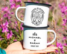 two white coffee mugs sitting on top of each other in front of purple flowers