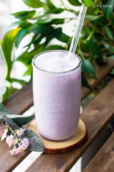 a glass filled with purple liquid sitting on top of a wooden table next to flowers