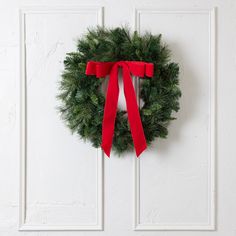 a green wreath with red ribbon hanging on a white door