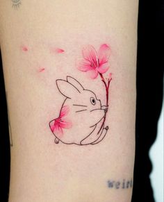 a small rabbit with pink flowers on it's back side tattoo by the artist