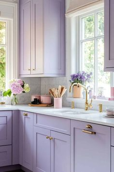 a kitchen with purple cabinets and white counter tops, gold pulls on the faucet